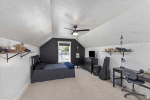 Carpeted bedroom featuring vaulted ceiling, a textured ceiling, a desk, ceiling fan, and baseboards