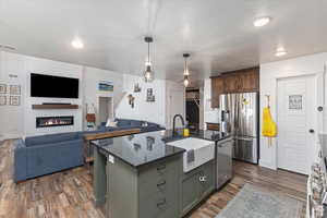 Kitchen featuring appliances with stainless steel finishes, a sink, dark wood-style flooring, dark stone counters, and open floor plan