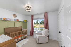 Bedroom featuring a nursery area, light colored carpet, baseboards, and a chandelier