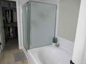Full bath with a stall shower, a garden tub, a walk in closet, and wood finished floors