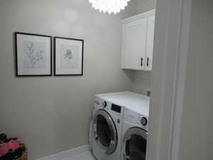 Washroom featuring separate washer and dryer, cabinet space, a chandelier, baseboards, and light tile patterned floors