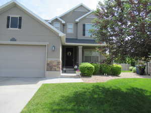 View of front of property with stucco siding, stone siding, driveway, and an attached garage