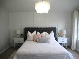 Carpeted bedroom featuring a decorative wall, a chandelier, and baseboards