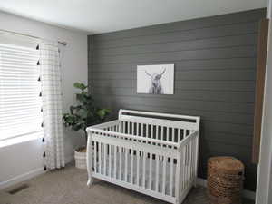 Carpeted bedroom featuring a crib, wooden walls, and baseboards