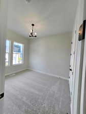 Spare room with light colored carpet and a chandelier