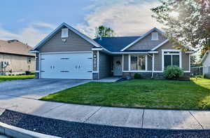 View of front facade featuring stone siding, a garage, concrete driveway, and a front yard