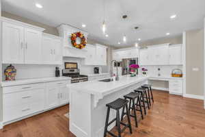 Kitchen with stainless steel appliances, a sink, decorative backsplash, a kitchen breakfast bar, and white cabinetry