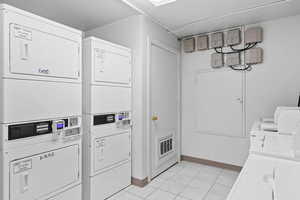 Community laundry room featuring stacked washing machine and dryer and baseboards