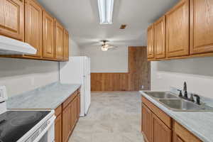 Kitchen featuring white appliances, a sink, wooden walls, a ceiling fan, and under cabinet range hood