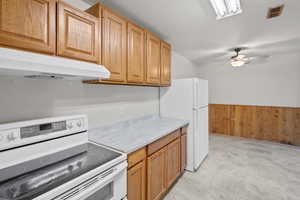 Kitchen featuring white appliances, under cabinet range hood, light countertops, ceiling fan, and a wainscoted wall