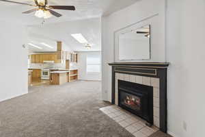 Unfurnished living room with light colored carpet, a skylight, a fireplace, baseboards, and vaulted ceiling