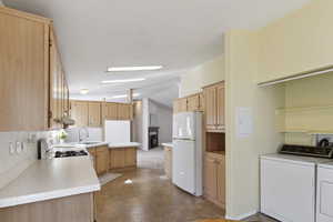 Kitchen with freestanding refrigerator, independent washer and dryer, range, vaulted ceiling, and light brown cabinetry