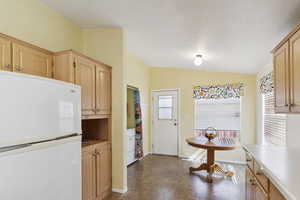 Kitchen featuring freestanding refrigerator, light brown cabinets, vaulted ceiling, dark floors, and washer / dryer