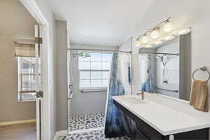 Bathroom with tiled shower, vanity, and baseboards