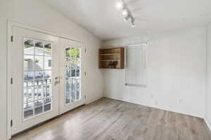 Spare room with light wood-style flooring, track lighting, baseboards, and french doors