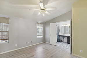 Unfurnished bedroom with lofted ceiling, wood finished floors, a sink, ensuite bath, and baseboards