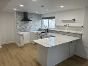 Kitchen with wall chimney exhaust hood, a sink, a peninsula, tasteful backsplash, and recessed lighting