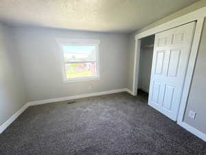 Unfurnished bedroom with a textured ceiling, dark colored carpet, and baseboards