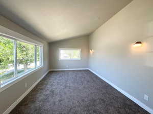 Empty room featuring lofted ceiling, dark colored carpet, baseboards, and a textured ceiling