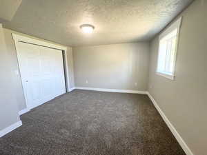 Unfurnished bedroom featuring a textured ceiling, dark carpet, baseboards, and a closet