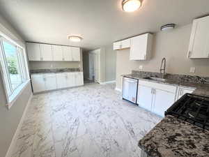 Kitchen featuring dishwasher, a sink, baseboards, light marble finish floors, and white cabinetry