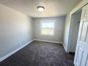 Empty room with a textured ceiling, dark carpet, and baseboards