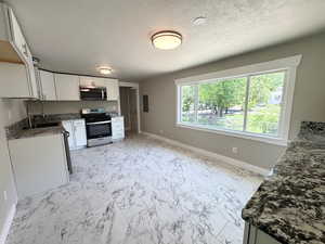 Kitchen with appliances with stainless steel finishes, a sink, baseboards, light marble finish flooring, and a textured ceiling