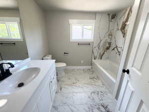 Full bath with vanity, marble finish floors, toilet, shower / washtub combination, and baseboards