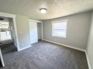 Unfurnished bedroom with dark carpet, a textured ceiling, baseboards, and a closet