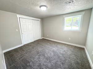 Unfurnished bedroom featuring carpet flooring, a textured ceiling, a closet, and baseboards