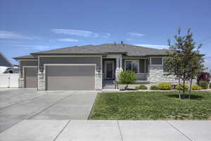 Prairie-style house featuring stone siding, a garage, driveway, a front yard, and stucco siding