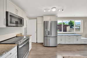 Kitchen featuring stainless steel appliances, light wood-style floors, light stone countertops, and white cabinetry