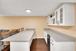 Kitchen featuring a peninsula, wine cooler, a kitchen bar, glass insert cabinets, and dark wood finished floors