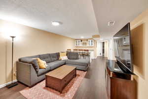 Living area featuring a textured ceiling, dark wood-style floors, and baseboards