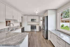 Kitchen featuring appliances with stainless steel finishes, a sink, white cabinets, and light wood-type flooring
