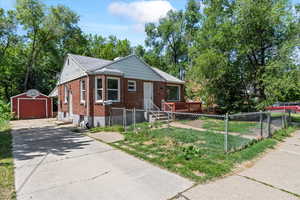 Bungalow-style home with brick siding, an outdoor structure, a fenced front yard, concrete driveway, and a detached garage