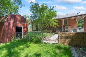 Rear view of house featuring an outdoor structure, a gambrel roof, brick siding, and ac unit