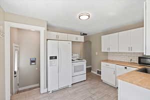 Kitchen featuring white appliances, arched walkways, baseboards, and white cabinetry