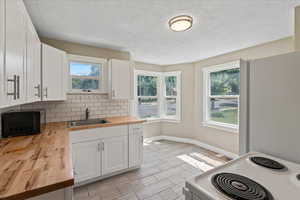 Kitchen featuring wooden counters, a sink, black microwave, baseboards, and stove