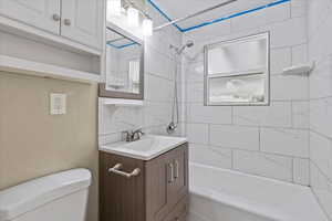 Bathroom with toilet, tub / shower combination, vanity, and decorative backsplash