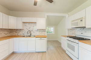 Kitchen featuring white appliances, butcher block countertops, a sink, light wood finished floors, and vaulted ceiling