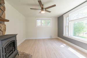 Unfurnished living room with a wood stove, a textured ceiling, light wood-type flooring, a ceiling fan, and healthy amount of natural light