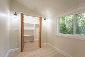 Hall with lofted ceiling, light wood-style flooring, a textured ceiling, and baseboards