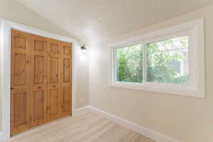 Unfurnished bedroom with a textured ceiling, lofted ceiling, light wood-style floors, baseboards, and a closet