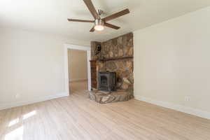 Unfurnished living room featuring a wood stove, ceiling fan, wood finished floors, a textured ceiling, and baseboards