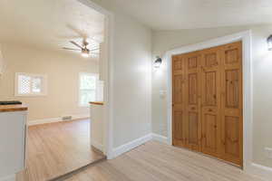 Entryway with light wood-style flooring, ceiling fan, a textured ceiling, lofted ceiling, and baseboards