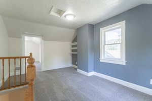 Bonus room with carpet, lofted ceiling, a textured ceiling, attic access, and baseboards