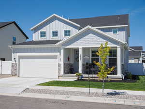 View of front of house featuring board and batten siding, a shingled roof, covered porch, driveway, and stone siding