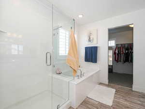 Bathroom with a shower stall, a bath, a spacious closet, wood finished floors, and baseboards