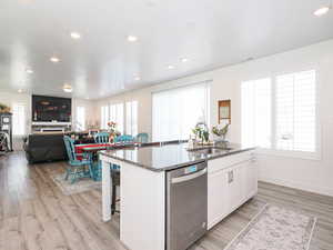 Kitchen featuring dishwasher, a sink, an island with sink, white cabinets, and dark stone countertops